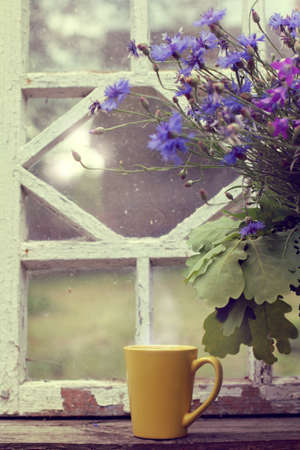 yellow mug and a large bouquet of wildflowers on the background of an old retro window / hot drink with the scent of summerの写真素材