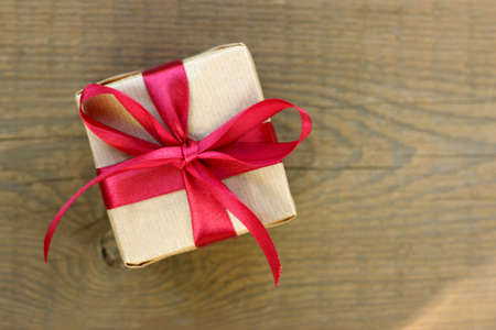 Gift tied with a red bow on a wooden table top view/ Universal surprise to any holidayの写真素材