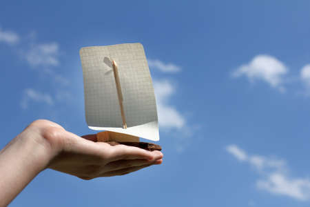 Homemade sailboat on hand against the sky with clouds / tailwind for your dreamsの写真素材