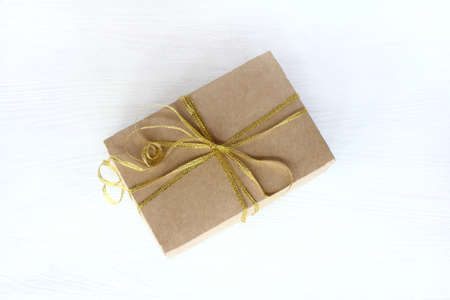 kraft box with bandaged gilded bow on a light table top view / Universal holiday surpriseの写真素材