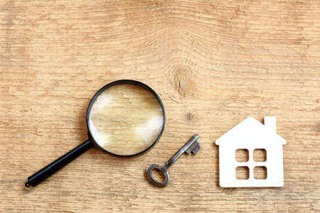 flat layout with a house, key and magnifying glass on a wooden surface top view / selection of retro real estateの写真素材