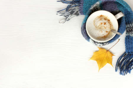flat lay with mug frothy cappuccino in blue scarf and maple leaf on table top view / warming coffee with autumnの写真素材