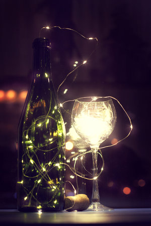 Bottle and glass filled with glowing lights garland table in the evening / imagination for romantic atmosphereの写真素材