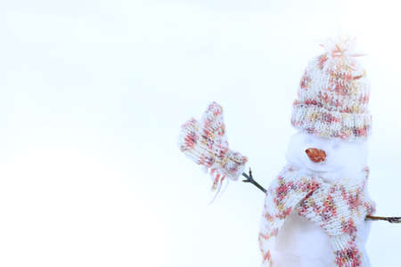 snowman dressed in warm clothes waving mitten on light background / good mood for winter vacationsの写真素材
