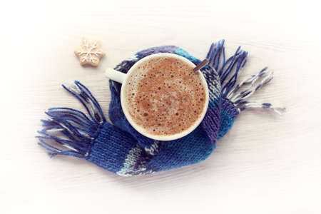 foamy cappuccino with cinnamon in white mug wrapped in blue scarf, next to Christmas cookie top view / fragrant winter coffeeの写真素材