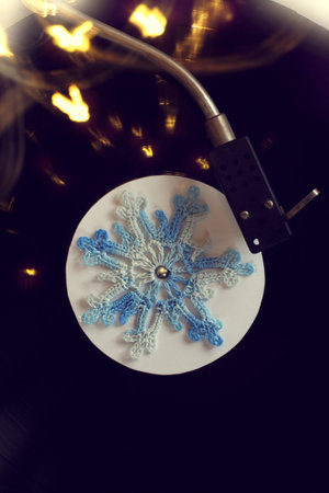 blue hand-knitted snowflake twists on the old vinyl plate in the player, top view / holiday songs...