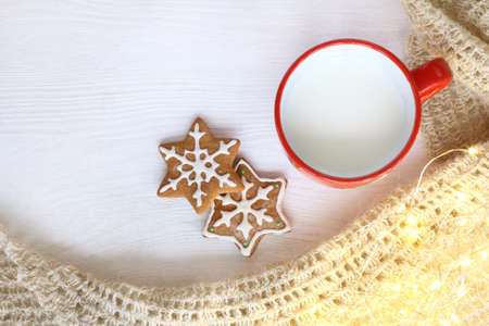 cup with milk and figured gingerbread cookies next to warm blanket and lights top view / drink for winter vacationの写真素材