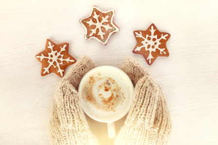 holiday cookies and a hot cup of cappuccino in the hands dressed in mittens/ warming drink for...