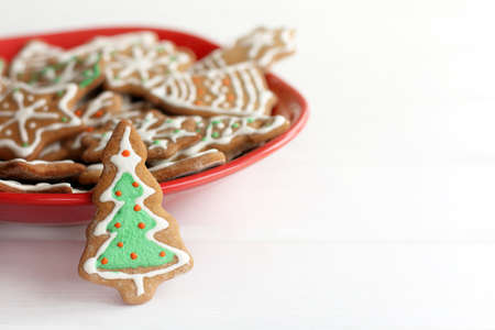 ginger glazed cookies in the shape of Christmas tree stands on table in red plate full of different pastries / appetizing atmosphere of winter holidaysの写真素材