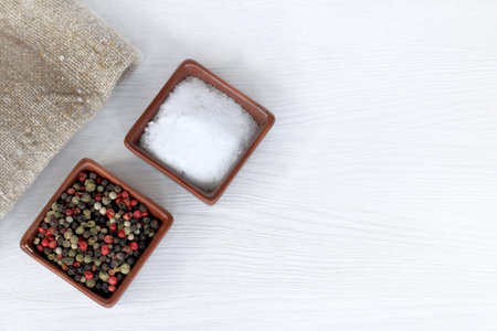 large salt and sweet pepper in colored peas on a light table top view / two important spices for the...
