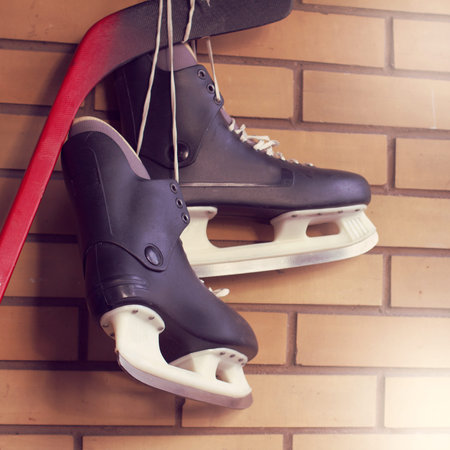 A pair of experienced skates hanging on a hockey stick against a wall / winter sports game