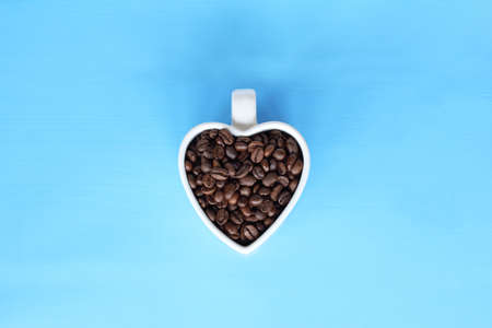 roasted coffee beans in a white cup on a blue table top view / the aroma of your favorite drinkの写真素材