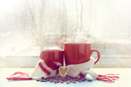 small and large red mug in scarf is decorated with cookie in the shape of heart on background  window after rain spring / together with your favorite coffee drinkの写真素材