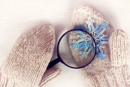 lying on a mitten a blue snowflake is viewed in a magnifying glass / winter which is knitted from a...