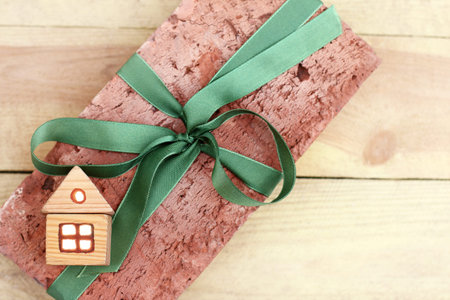 wooden model house on the background of oven bricks with festive ribbon top view / ecological materials for comfortable livingの写真素材