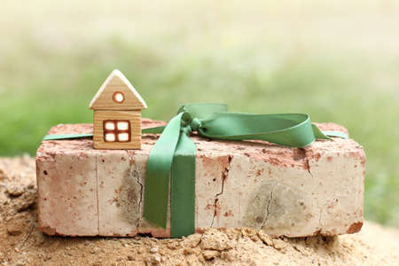 model of a wooden house stands on a gift brick on a sandy mountain / ecological materials for comfortの写真素材