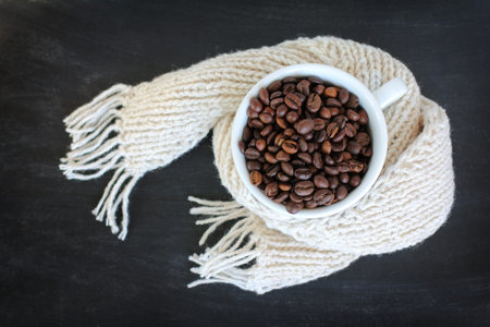 cup filled with roasted coffee beans wrapped in a scarf top view / warming aromatic drink