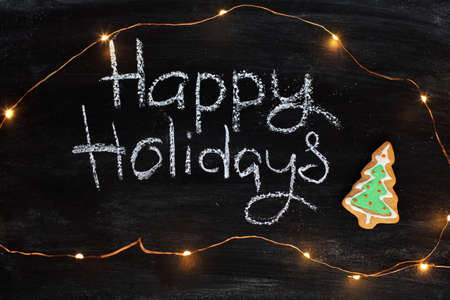 inscription in chalk happy holiday surrounded by lights of garland and cookies / flavor eventsの写真素材