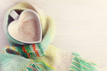 frothy cappuccino in the shape of a heart pour into a mug wrapped with a scarf top view / warming coffee breakの写真素材