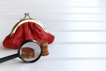 stacks of coins with a magnifying glass and a red wallet on the table, front view / keeping accurate records in businessの写真素材