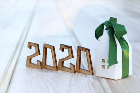 paper house layout is wrapped in a gift ribbon next to a wooden number indicating the year. concept...