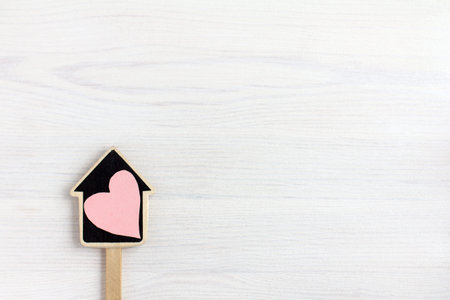 Layout of a house on a stick with a heart symbol on a light wooden background.  home sweetheart...