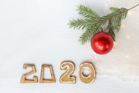 red ball and a sprig of a Christmas tree on a table with garland lights and the number 2020....
