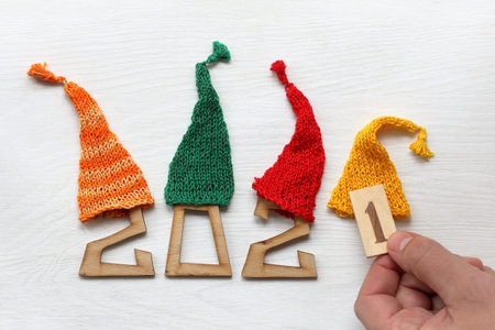 wooden figures in multi-colored knitted caps and a hand with the number one. upcoming holidays 2021