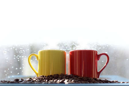 red and yellow mug with coffee beans and white steam on top. hot spot for inscriptionの写真素材