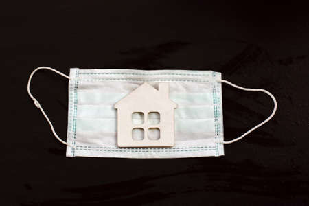 model of the house on a background of a medical mask on a dark background. individual isolation conceptの写真素材