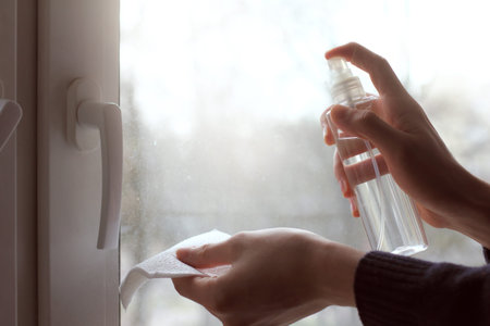 bottle with a disinfectant liquid and a napkin in hands on a window background. surface treatment...