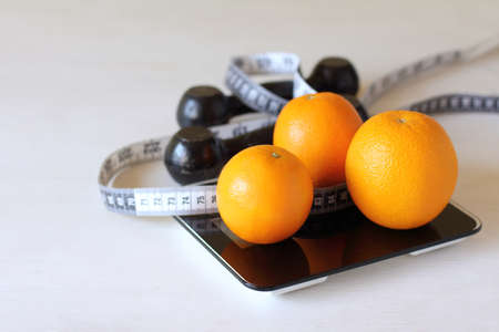 oranges, a centimeter ruler and dumbbells on the scales. fruits and exercise for healthの写真素材