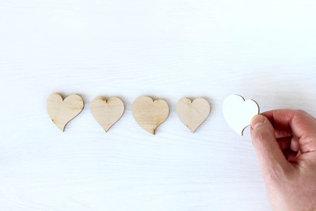 hand adds white heart symbol to four wooden ones on table top view. new follower increases rating