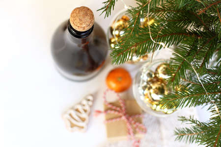 in the foreground sharply cork in a bottle and spruce paws with a garland on the background of blurry glasses with balls, a gift and a tangerine with cookies on a table top view. holiday anticipation of the new yearの写真素材