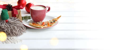 gnome in a green cap on the background of pizza dishes and a cup of coffee with a gift and decorations. Warming breakfasts for winter breaksの写真素材