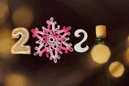 curly gingerbread, knitted snowflake, number two and a bottle of sparkling wine, with lights of illumination on a dark background. celebrating the new year 2021の写真素材