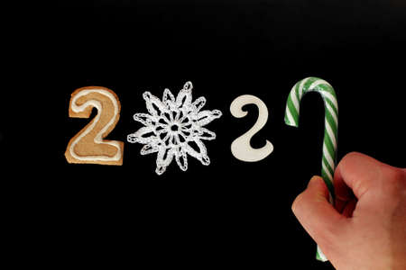 curly gingerbread, knitted snowflake, number two and striped candy in hand on dark background. offensive the new year 2021の写真素材