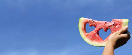 red slice of watermelon with holes in the shape of hearts against the blue sky. favorite season is summerの写真素材