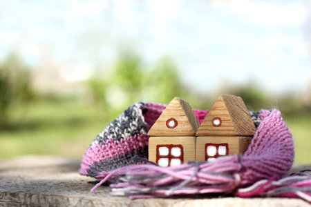 pair of wooden houses wrapped together in a warm scarf on a blurred landscape background. cozy locked family homeの写真素材