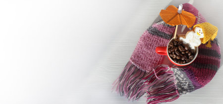 in a cup full of coffee beans a gingerbread snowman sits under an umbrella against the background of a table with a knitted scarf top view. cozy winter weekendの写真素材
