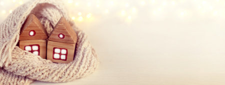 two wooden houses together wrapped in a light knitted scarf on the background of garlands lights. winter holidays in retro styleの写真素材