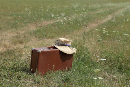 large leather suitcase and an old straw hat with a small lavender bouquet in a field by a country road. summer retro ecotourismの写真素材
