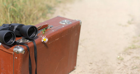 retro suitcase, chamomile flower and binoculars on the background of the road. romance of distant wanderingsの写真素材