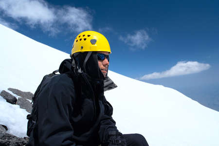 young hiker in glasses posing and mountainside with blue sky in the backgroundの写真素材