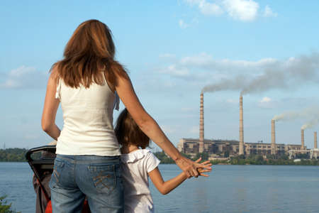 "care future" concept. Young mother with her kids are looking at the chimney-stalks polluting an airの写真素材