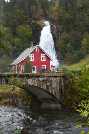 traditional norwagian wooden house and old arch bridge with waterfall in the distanceの写真素材