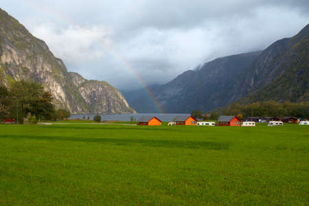 green meadow with houses  on a fjord coast and mountains  with rainbow in the distance, norway
の写真素材