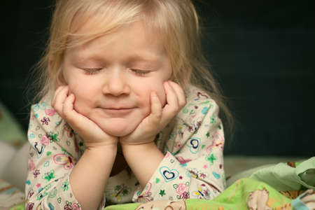 smiling child with shutted eyes lying on her bedの写真素材