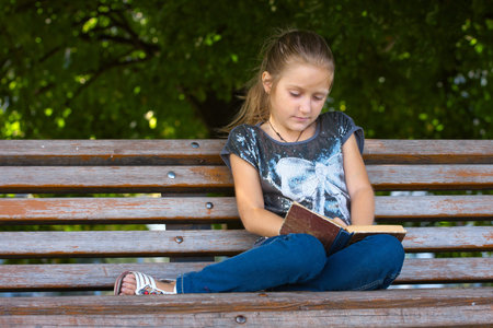 little girl sitting on a bench at the park and reading