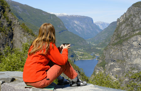girl hiker on a rest holding a cup of tea and looking at the fjordの写真素材